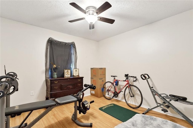 exercise room featuring a textured ceiling, ceiling fan, and wood finished floors
