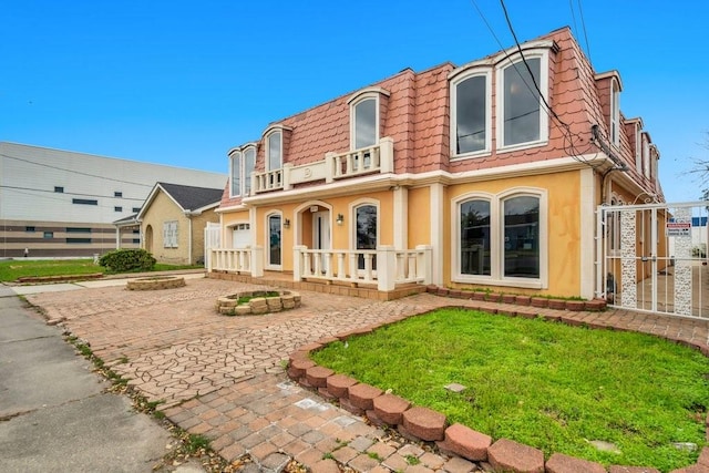 back of property featuring fence, a balcony, stucco siding, mansard roof, and a porch