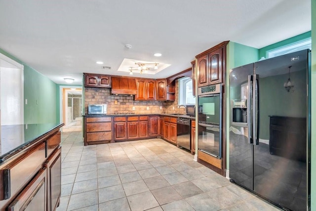 kitchen featuring brown cabinetry, a sink, backsplash, light tile patterned floors, and black appliances