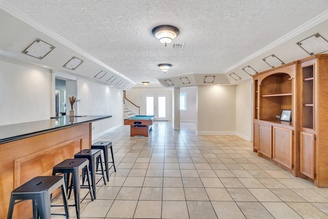 interior space featuring visible vents, baseboards, a kitchen bar, a textured ceiling, and light tile patterned floors