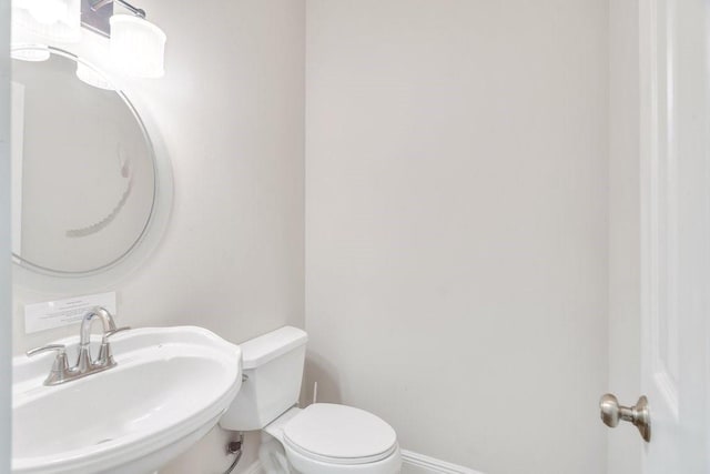 half bathroom with baseboards, a sink, and toilet
