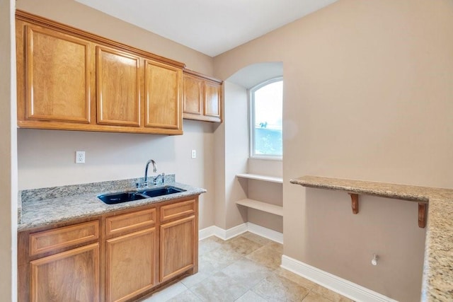 kitchen featuring light stone counters, a sink, arched walkways, baseboards, and light tile patterned floors
