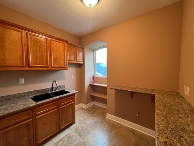 kitchen with brown cabinetry, baseboards, arched walkways, a sink, and light tile patterned floors