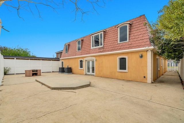 rear view of property with a tiled roof, french doors, mansard roof, a patio, and stucco siding