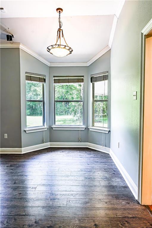 unfurnished dining area with crown molding, dark wood-style flooring, and baseboards