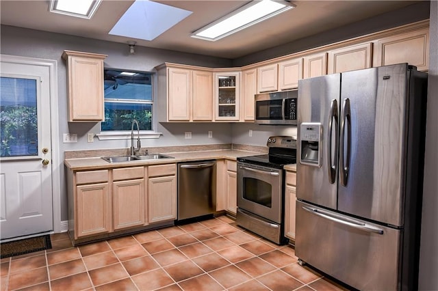 kitchen with glass insert cabinets, light countertops, a sink, appliances with stainless steel finishes, and light tile patterned floors