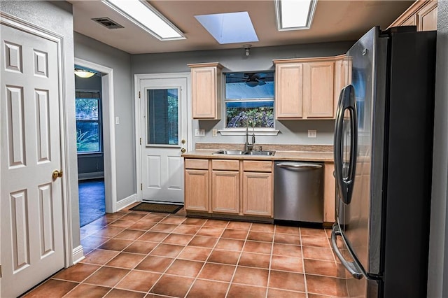 kitchen with light brown cabinets, tile patterned floors, a sink, appliances with stainless steel finishes, and a skylight