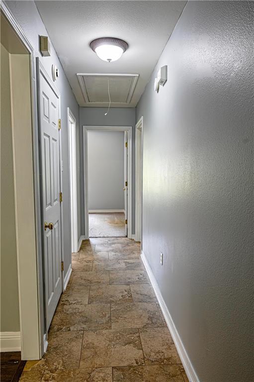 hall with baseboards, attic access, and stone tile flooring