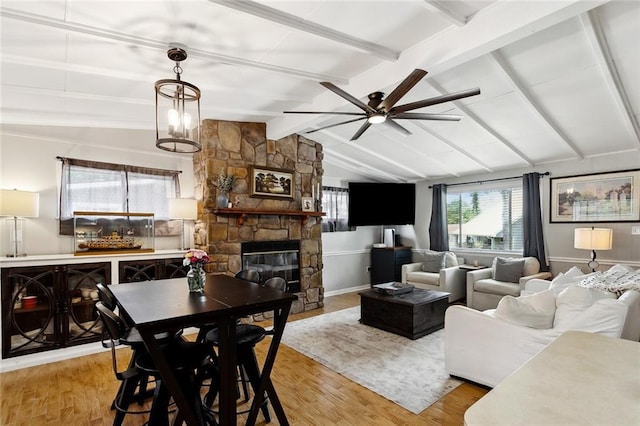living room with a stone fireplace, lofted ceiling with beams, light wood-style flooring, and a ceiling fan