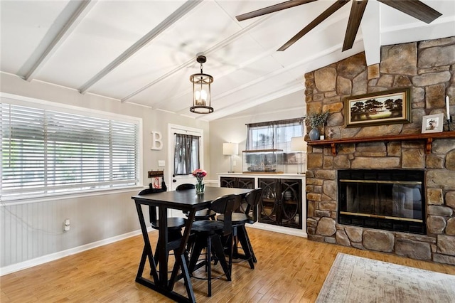 dining area featuring a ceiling fan, a fireplace, wood finished floors, baseboards, and lofted ceiling with beams