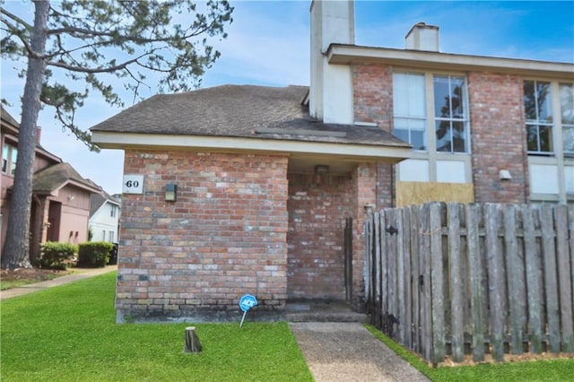 view of side of property with a yard, brick siding, fence, and a chimney