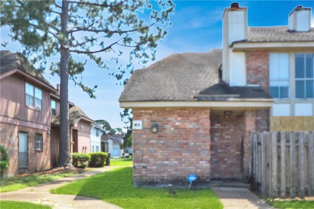 view of home's exterior featuring brick siding, fence, a yard, and a chimney