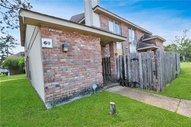 view of home's exterior featuring a lawn, brick siding, fence, and a chimney