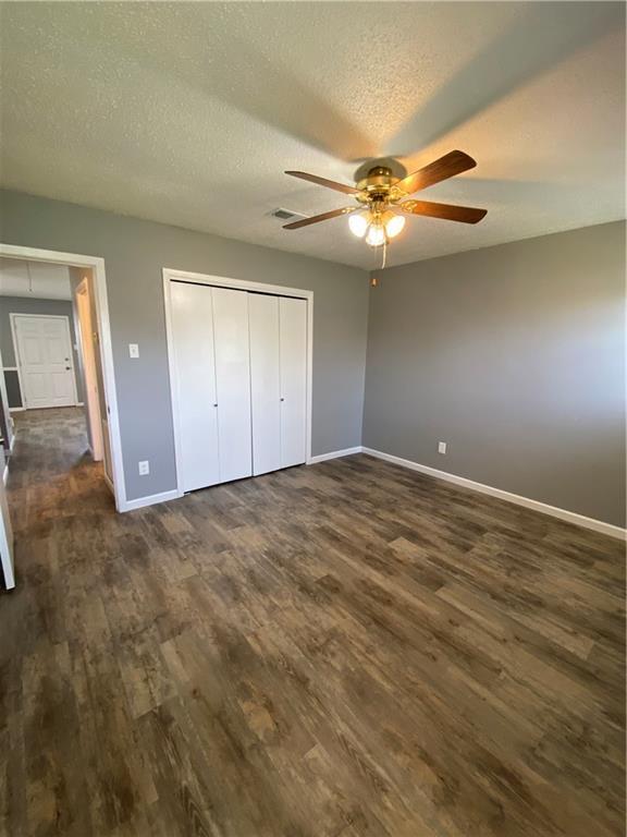 unfurnished bedroom with baseboards, a textured ceiling, dark wood-style flooring, and a closet