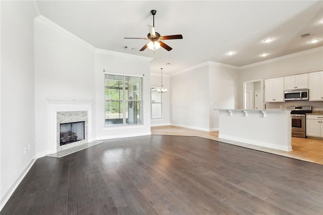 unfurnished living room featuring a high end fireplace, ceiling fan with notable chandelier, light wood finished floors, and visible vents