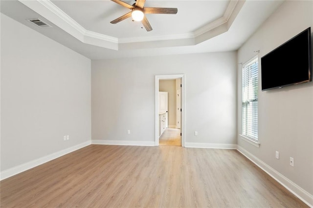 spare room featuring a ceiling fan, visible vents, a raised ceiling, light wood finished floors, and ornamental molding
