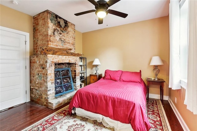 bedroom with baseboards, a ceiling fan, a brick fireplace, and wood finished floors
