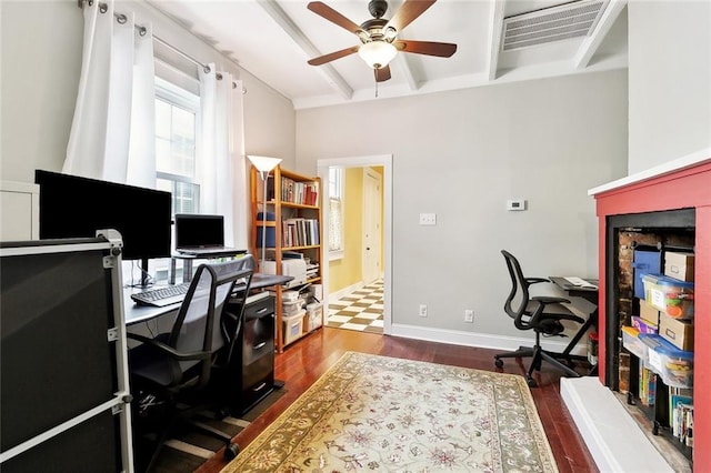 office area with beam ceiling, a fireplace with raised hearth, a ceiling fan, wood finished floors, and visible vents