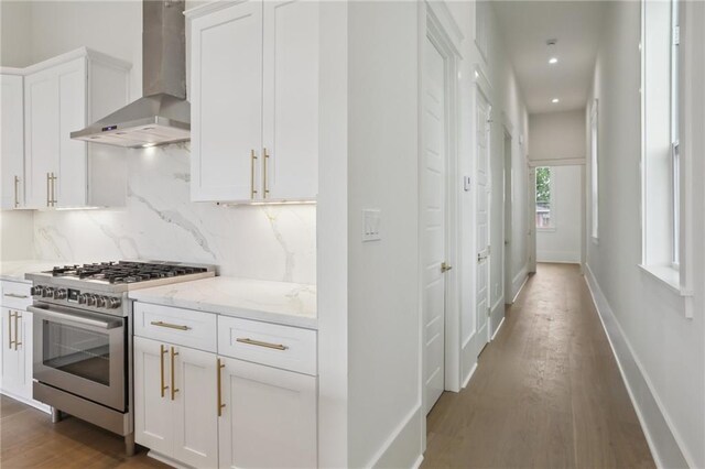 537 Thayer St, New Orleans, LA 70114 - kitchen with wall chimney range hood, white cabinets, stainless steel gas range oven, backsplash, and dark wood-style floors