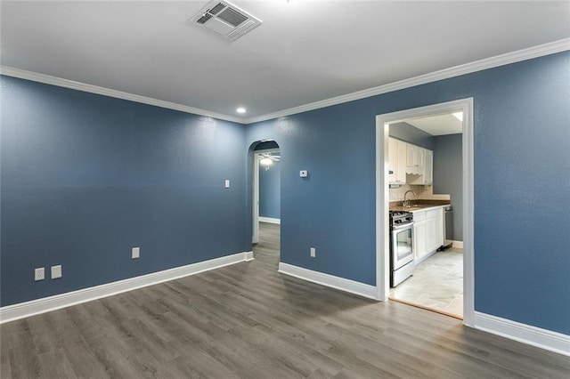 empty room with light wood-style floors, arched walkways, baseboards, visible vents, and ornamental molding