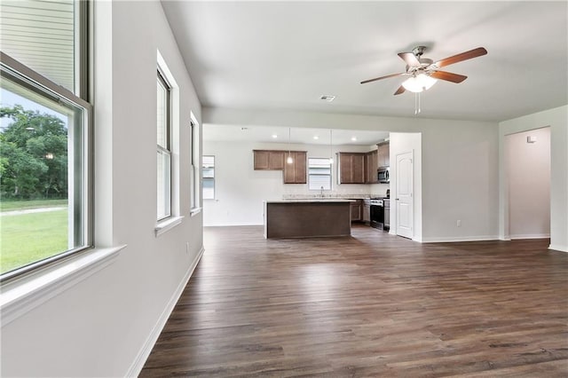 unfurnished living room with a sink, baseboards, a ceiling fan, and a healthy amount of sunlight