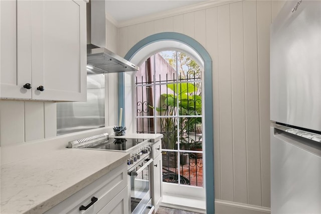 415 Burgundy St Unit 1B, New Orleans, LA 70112 - kitchen featuring wall chimney exhaust hood, appliances with stainless steel finishes, crown molding, white cabinetry, and light stone counters