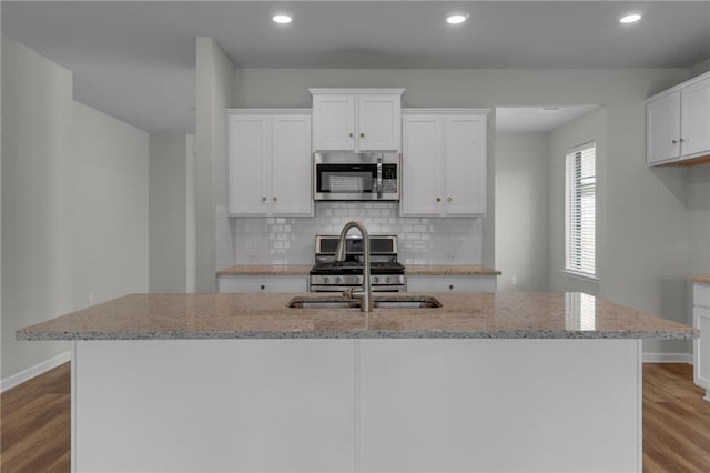 kitchen with stainless steel appliances, a sink, baseboards, a center island with sink, and recessed lighting