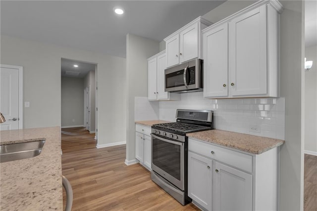 kitchen featuring appliances with stainless steel finishes, a sink, baseboards, backsplash, and white cabinets