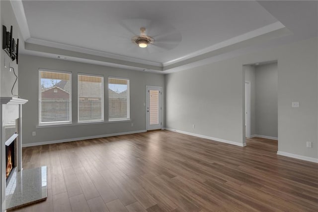 unfurnished living room featuring a tray ceiling, a high end fireplace, a ceiling fan, wood finished floors, and baseboards