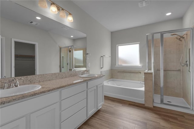 full bathroom with a shower stall, a bath, wood finished floors, a walk in closet, and double vanity