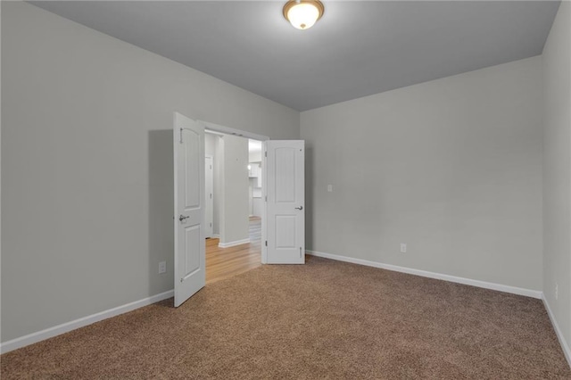 spare room featuring light colored carpet and baseboards