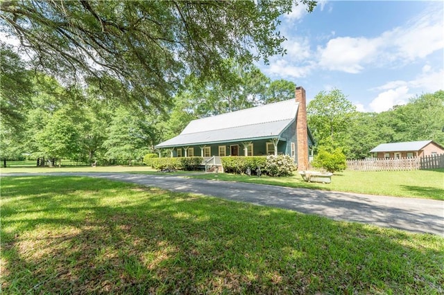 view of front of house featuring fence, a front lawn, a chimney, covered porch, and metal roof