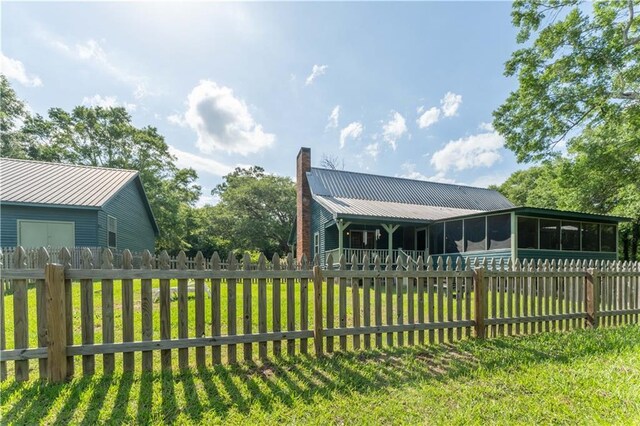 exterior space with metal roof, a chimney, a sunroom, a fenced backyard, and a yard