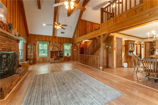 unfurnished living room featuring a fireplace, wood finished floors, high vaulted ceiling, beamed ceiling, and ceiling fan with notable chandelier