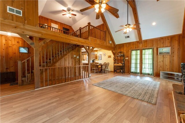 unfurnished living room featuring stairway, ceiling fan, wood walls, and visible vents