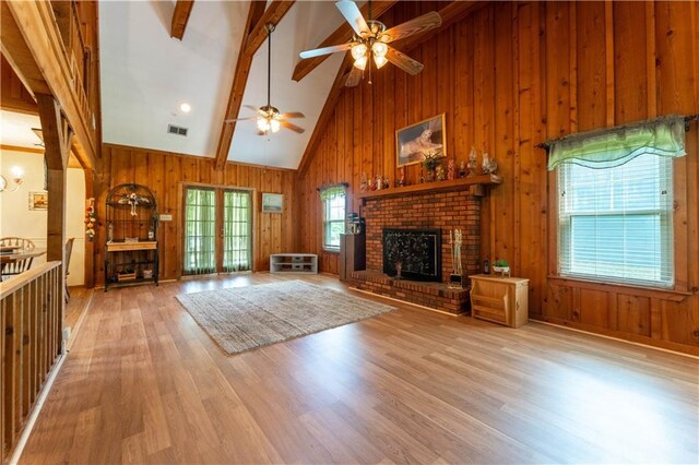 unfurnished living room with wooden walls, a ceiling fan, wood finished floors, beamed ceiling, and visible vents