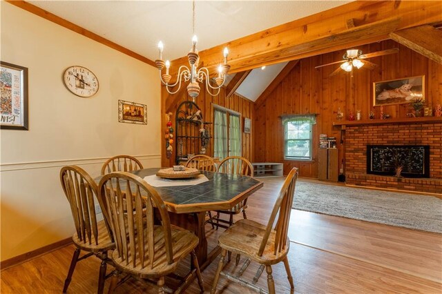 dining room featuring wood finished floors, a fireplace, wooden walls, lofted ceiling with beams, and ceiling fan with notable chandelier