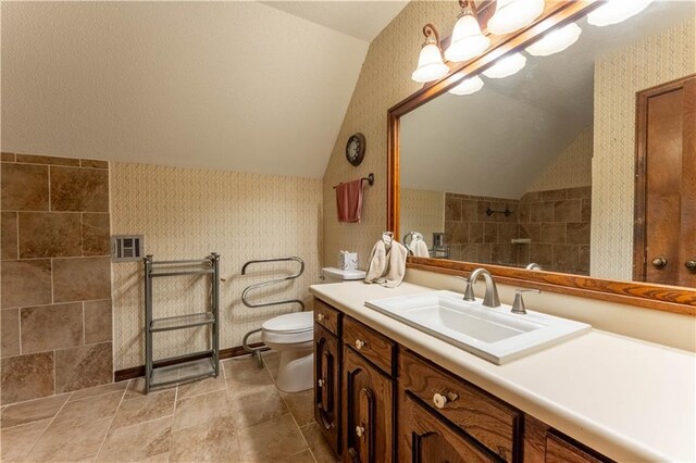 full bathroom featuring a tile shower, vaulted ceiling, vanity, toilet, and wallpapered walls
