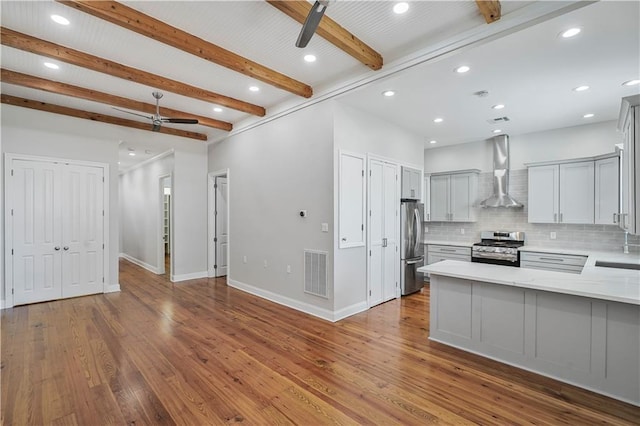 kitchen featuring wall chimney exhaust hood, stainless steel appliances, a ceiling fan, tasteful backsplash, and visible vents