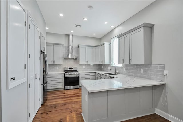 kitchen featuring a peninsula, gray cabinets, wall chimney exhaust hood, a sink, and stainless steel appliances
