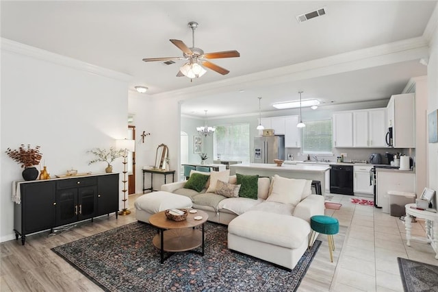 living area featuring light wood-style floors, ornamental molding, ceiling fan with notable chandelier, and visible vents