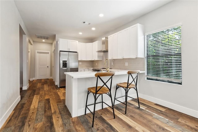 kitchen featuring a peninsula, visible vents, stainless steel fridge, and wall chimney exhaust hood