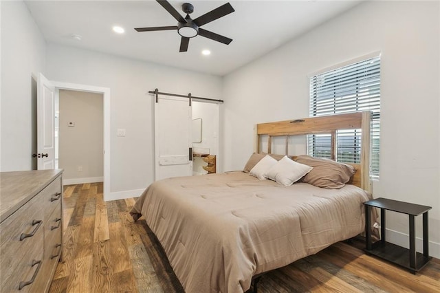 bedroom featuring ceiling fan, a barn door, wood finished floors, baseboards, and recessed lighting