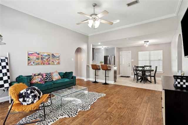 living area with arched walkways, a ceiling fan, wood finished floors, visible vents, and ornamental molding