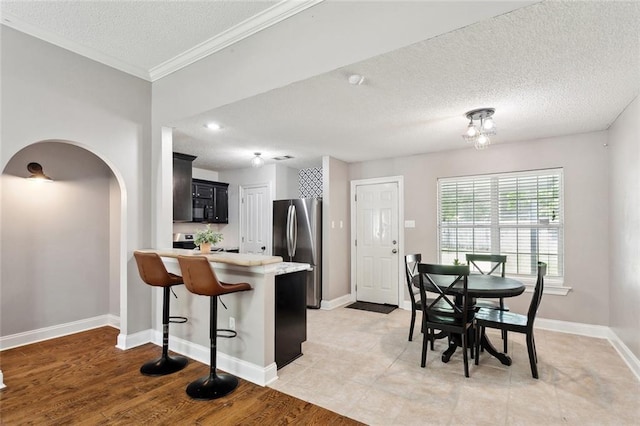 kitchen featuring a textured ceiling, appliances with stainless steel finishes, arched walkways, light countertops, and dark cabinets