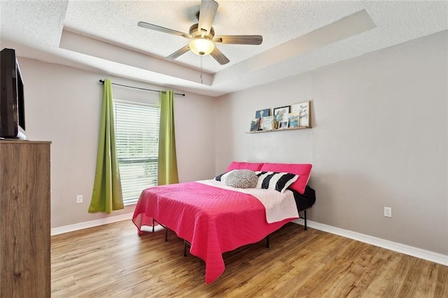 bedroom with a textured ceiling, wood finished floors, and a tray ceiling