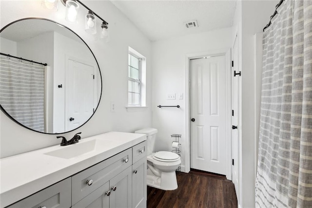 full bath featuring vanity, toilet, wood finished floors, and visible vents