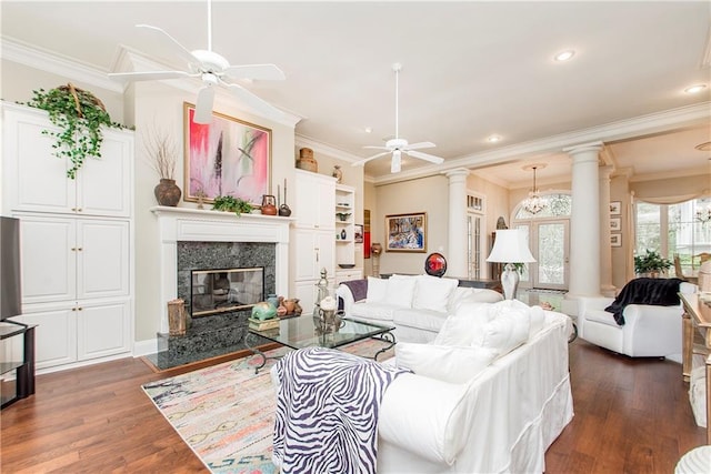 living room featuring a ceiling fan, ornamental molding, wood finished floors, decorative columns, and a fireplace