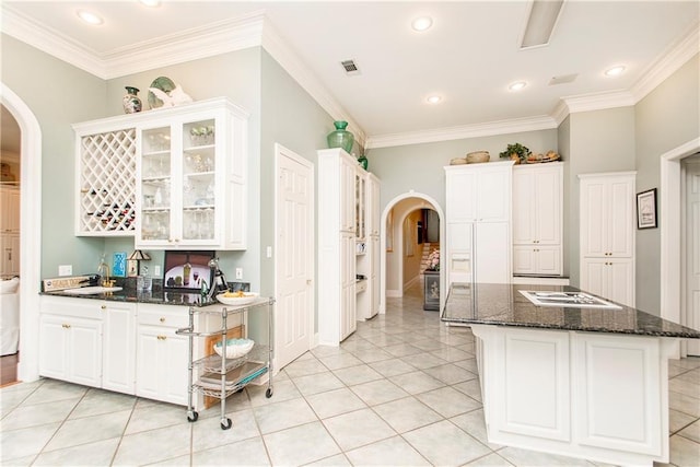 kitchen with arched walkways, ornamental molding, white cabinets, glass insert cabinets, and recessed lighting