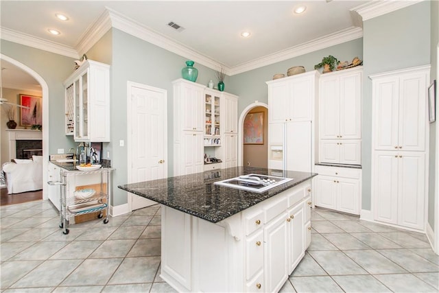 kitchen featuring arched walkways, white cooktop, light tile patterned floors, white cabinetry, and glass insert cabinets